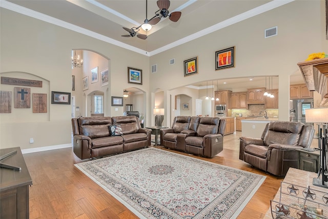 living room with ornamental molding, ceiling fan with notable chandelier, and light hardwood / wood-style flooring