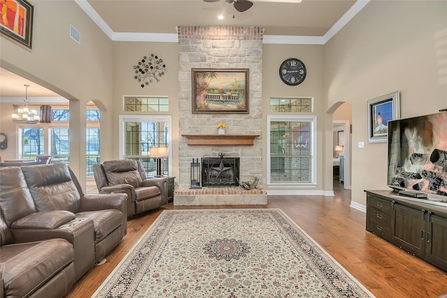 living room featuring a healthy amount of sunlight, ornamental molding, a stone fireplace, and light wood-type flooring