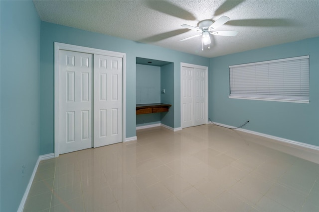 unfurnished bedroom featuring multiple closets, ceiling fan, built in desk, and a textured ceiling