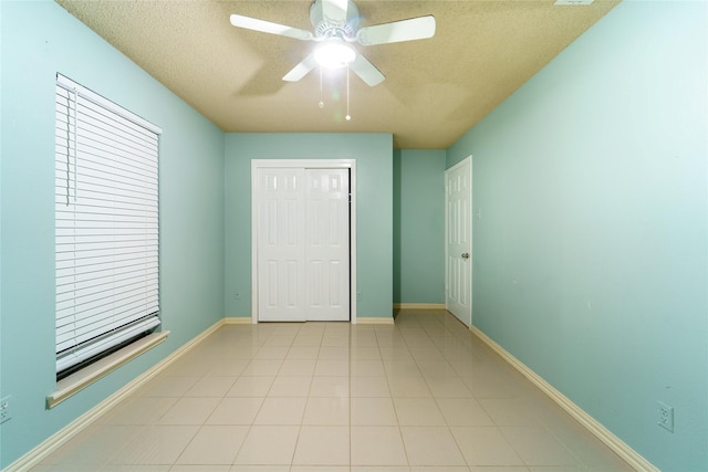 unfurnished bedroom with light tile patterned flooring, ceiling fan, a closet, and a textured ceiling