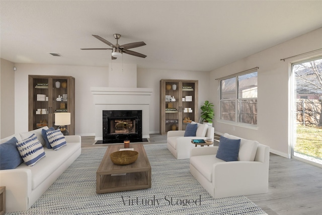 living area featuring baseboards, visible vents, a fireplace with flush hearth, ceiling fan, and wood finished floors