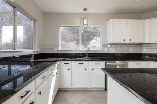 kitchen with dark stone countertops, a sink, decorative light fixtures, and white cabinets