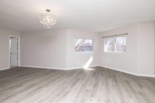 spare room with an inviting chandelier and light hardwood / wood-style floors