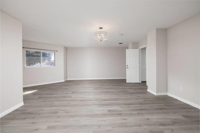 spare room with baseboards, wood finished floors, and an inviting chandelier