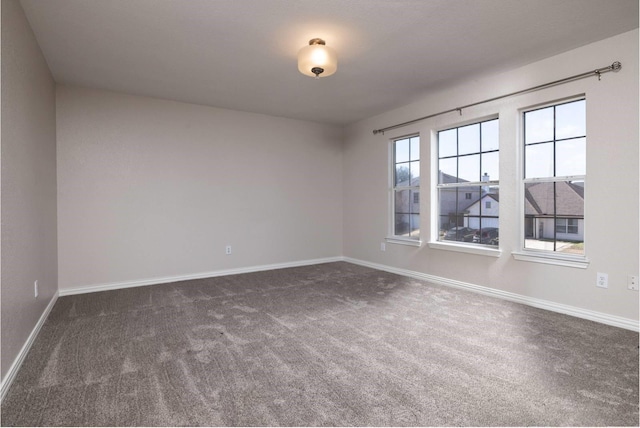 spare room featuring dark carpet and baseboards