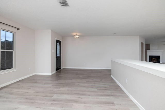 spare room featuring light wood-type flooring, visible vents, a fireplace, and baseboards