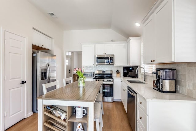 kitchen with appliances with stainless steel finishes, white cabinetry, sink, decorative backsplash, and light hardwood / wood-style floors