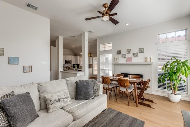 living room with ceiling fan, lofted ceiling, light hardwood / wood-style floors, and a brick fireplace