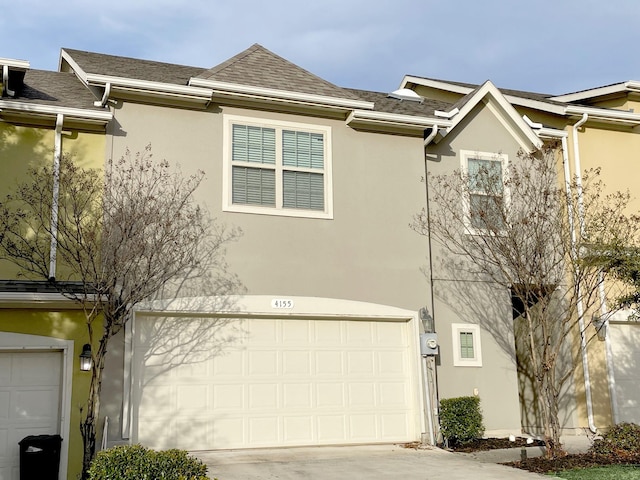 view of property featuring a garage, roof with shingles, driveway, and stucco siding