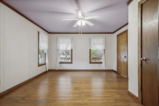 empty room featuring crown molding, ceiling fan, wood-type flooring, and plenty of natural light