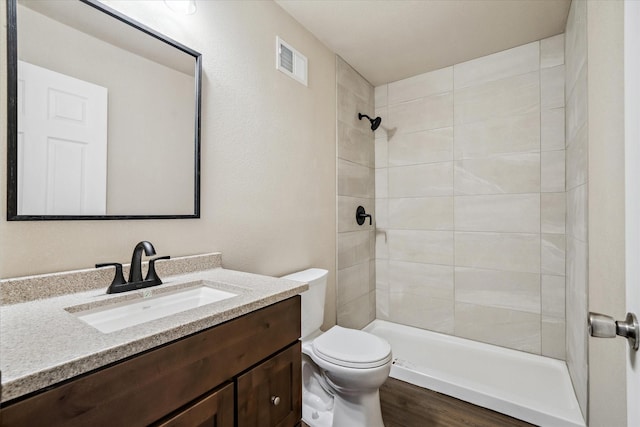 bathroom with tiled shower, vanity, toilet, and hardwood / wood-style floors