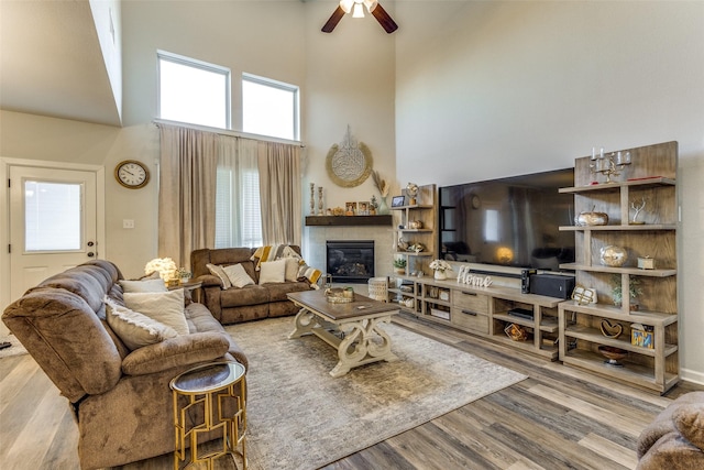 living room with a high ceiling, a tile fireplace, ceiling fan, and light wood-type flooring