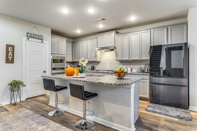 kitchen with appliances with stainless steel finishes, a kitchen breakfast bar, a kitchen island with sink, and wood-type flooring