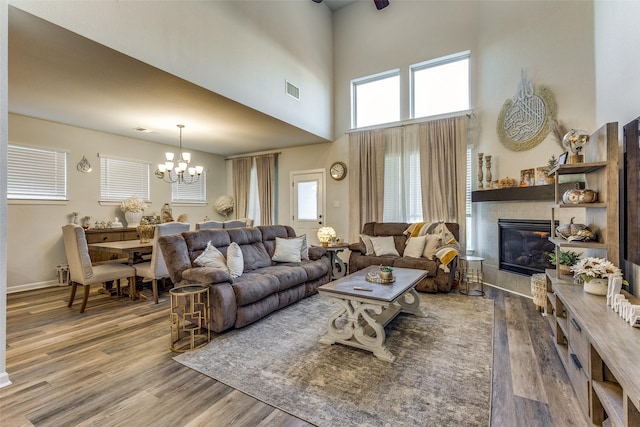 living room featuring a notable chandelier, hardwood / wood-style flooring, a fireplace, and a towering ceiling