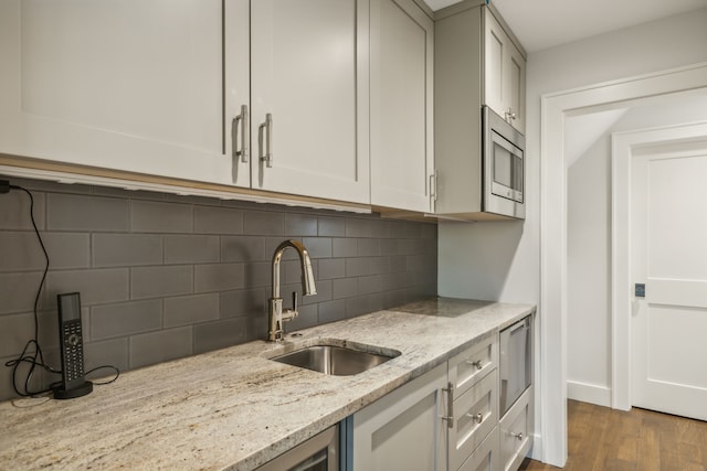 kitchen featuring sink, light hardwood / wood-style flooring, stainless steel microwave, light stone counters, and decorative backsplash