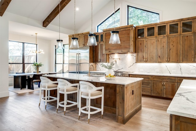 kitchen with sink, stainless steel built in fridge, an island with sink, pendant lighting, and backsplash