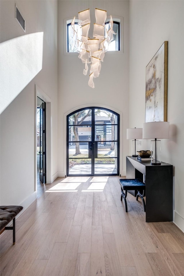 foyer with french doors, an inviting chandelier, light hardwood / wood-style floors, and a high ceiling