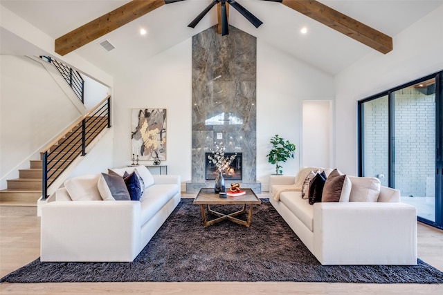 living room featuring a tiled fireplace, light hardwood / wood-style flooring, high vaulted ceiling, and beamed ceiling