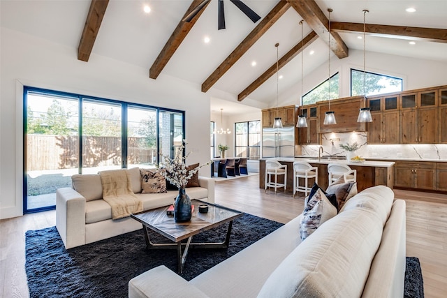 living room with a healthy amount of sunlight, high vaulted ceiling, a chandelier, and light wood-type flooring