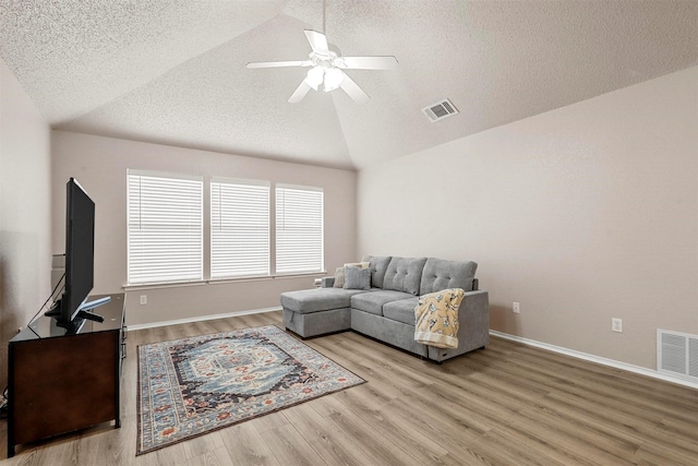 living room with ceiling fan, lofted ceiling, a textured ceiling, and light hardwood / wood-style floors