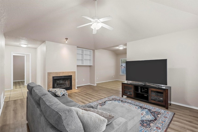 living room featuring hardwood / wood-style flooring, ceiling fan, a textured ceiling, a tiled fireplace, and vaulted ceiling