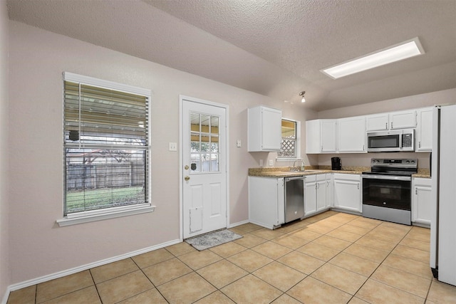 kitchen with lofted ceiling, sink, light tile patterned floors, appliances with stainless steel finishes, and white cabinets