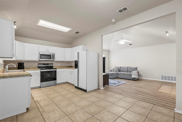 kitchen with sink, vaulted ceiling, white cabinets, and appliances with stainless steel finishes