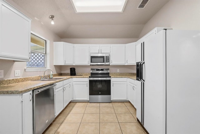 kitchen with lofted ceiling, sink, light tile patterned floors, white cabinetry, and stainless steel appliances