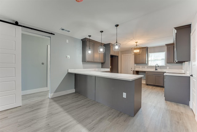 kitchen featuring pendant lighting, sink, light hardwood / wood-style floors, kitchen peninsula, and a barn door