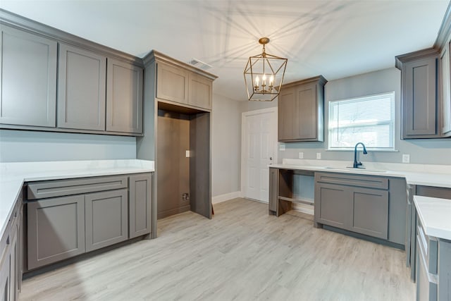 kitchen featuring gray cabinetry, sink, decorative light fixtures, and light hardwood / wood-style floors