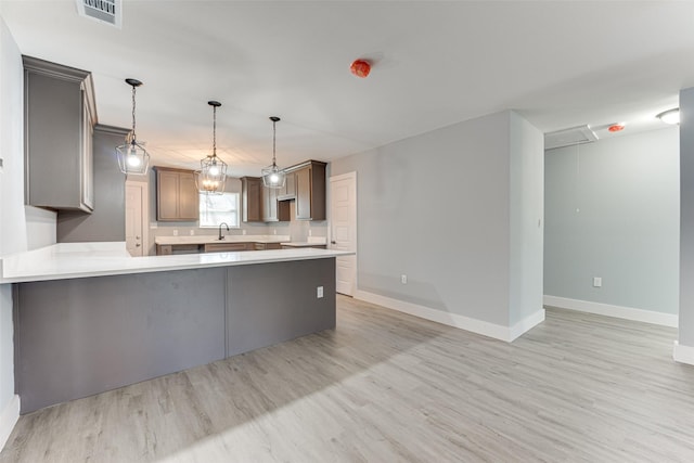 kitchen featuring kitchen peninsula, sink, hanging light fixtures, and light hardwood / wood-style flooring