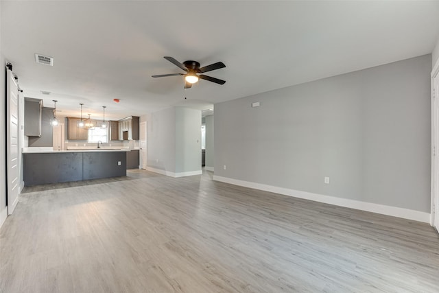 unfurnished living room featuring a barn door, ceiling fan, sink, and hardwood / wood-style floors