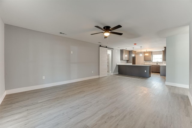 unfurnished living room with sink, a barn door, ceiling fan, and light wood-type flooring