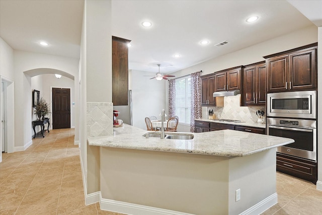 kitchen with light stone counters, appliances with stainless steel finishes, kitchen peninsula, and sink