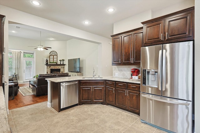 kitchen featuring sink, dark brown cabinets, stainless steel appliances, tasteful backsplash, and a stone fireplace