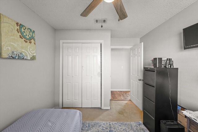 carpeted bedroom with a closet, ceiling fan, and a textured ceiling