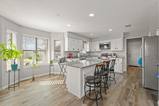 kitchen featuring appliances with stainless steel finishes, white cabinets, a breakfast bar area, and a center island