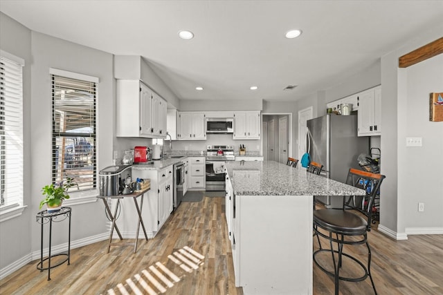 kitchen with appliances with stainless steel finishes, a kitchen bar, light stone counters, a center island, and white cabinets