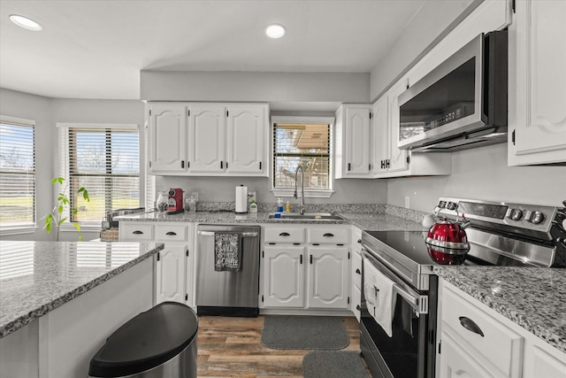 kitchen with white cabinetry, stainless steel appliances, sink, a healthy amount of sunlight, and light stone counters