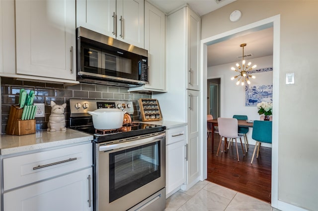 kitchen with stainless steel appliances, white cabinetry, light stone countertops, and backsplash