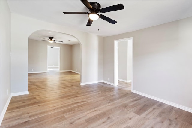 empty room with light wood-style floors, baseboards, and arched walkways