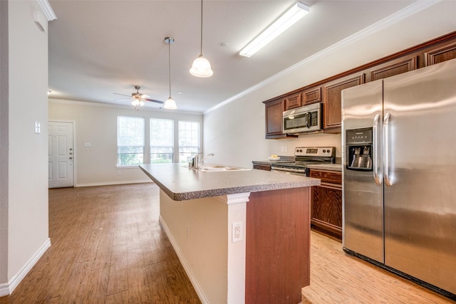 kitchen with hanging light fixtures, a center island with sink, ornamental molding, and appliances with stainless steel finishes