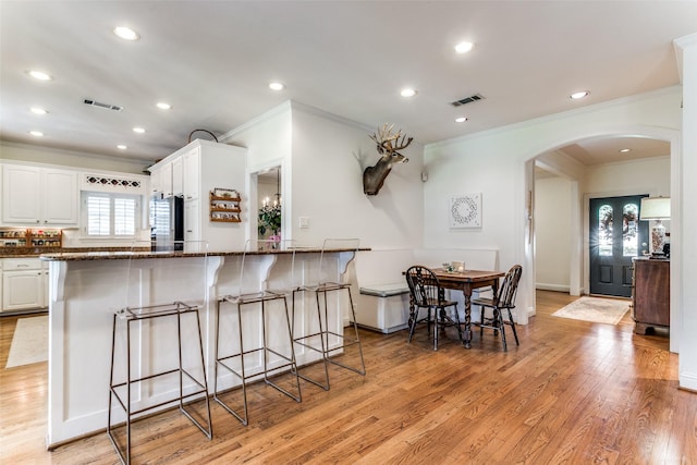 kitchen featuring stainless steel refrigerator, white cabinetry, dark stone countertops, light hardwood / wood-style floors, and a kitchen bar