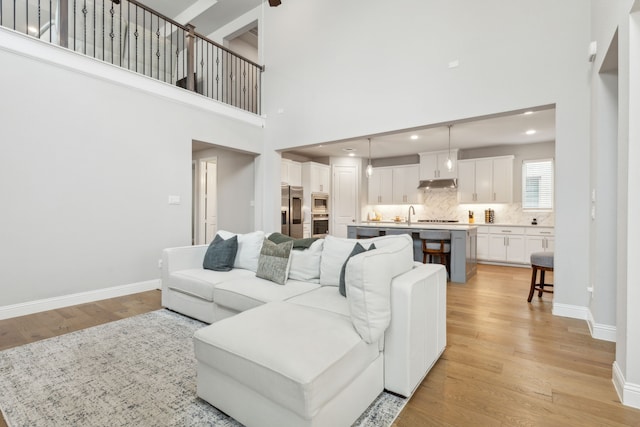 living area featuring recessed lighting, light wood-type flooring, baseboards, and a towering ceiling