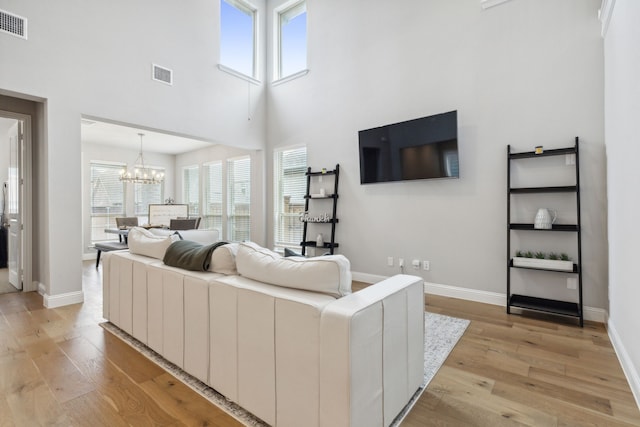 living area featuring visible vents, light wood-style flooring, plenty of natural light, and an inviting chandelier