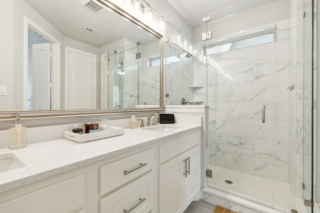 bathroom with a marble finish shower, visible vents, double vanity, and a sink