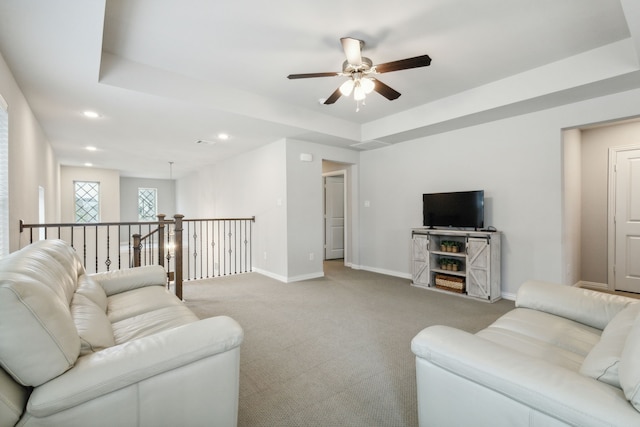 living area featuring a tray ceiling, recessed lighting, baseboards, light colored carpet, and ceiling fan