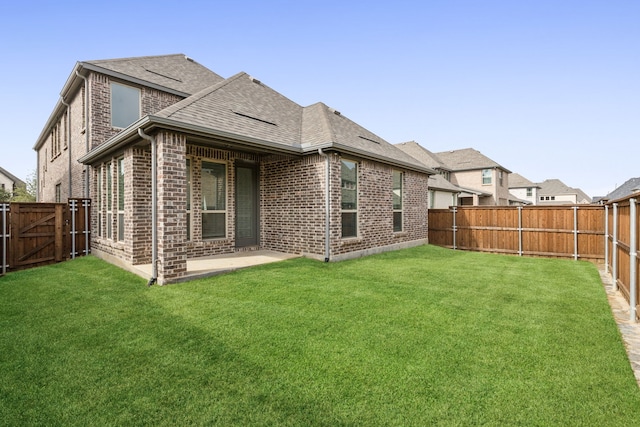 rear view of property with a yard, a patio, brick siding, and roof with shingles