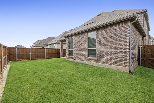 rear view of property featuring brick siding, a fenced backyard, and a lawn