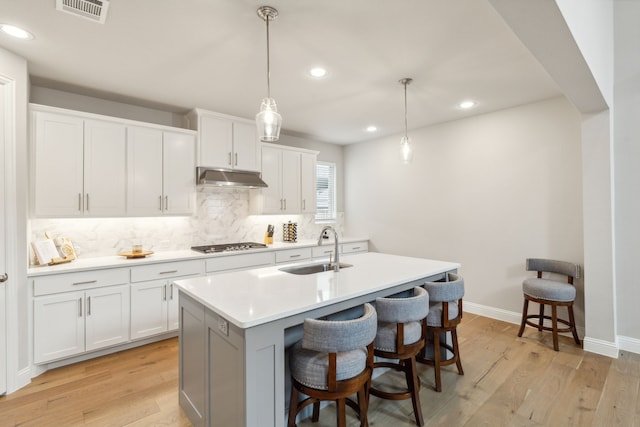 kitchen with visible vents, light wood-style flooring, a sink, under cabinet range hood, and stainless steel gas stovetop